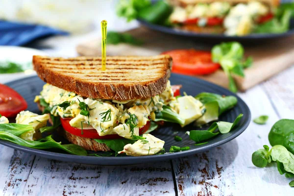 Egg salad sandwich with a cocktail stick on a black plate.