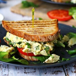 Egg salad sandwich on a black plate with dill garnish and lettuce around it.