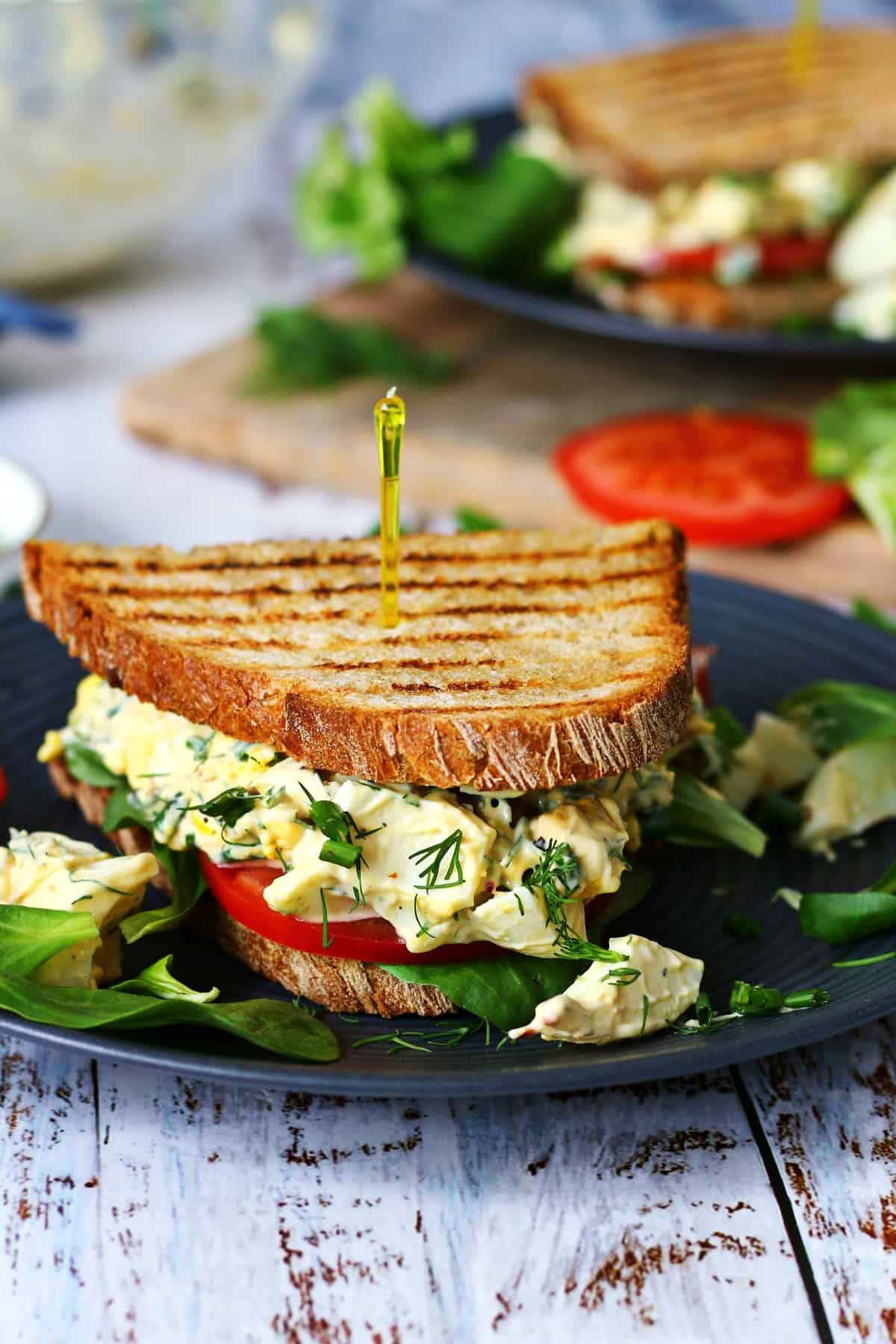 Egg salad sandwich on a black plate with lamb's lettuce for decoration and another sandwich at the back.