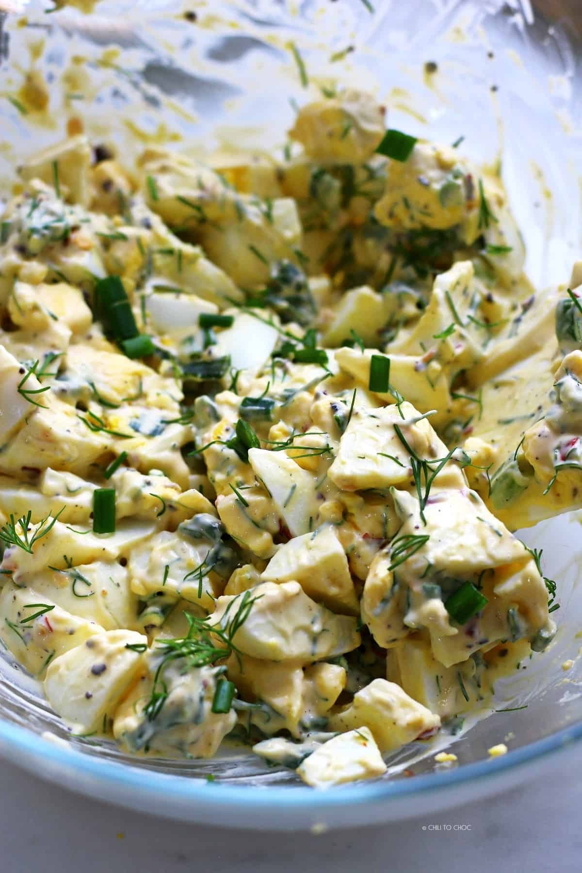 Chopped hard boiled eggs mixed with mayonnaise, chives and dill in a transparent bowl.