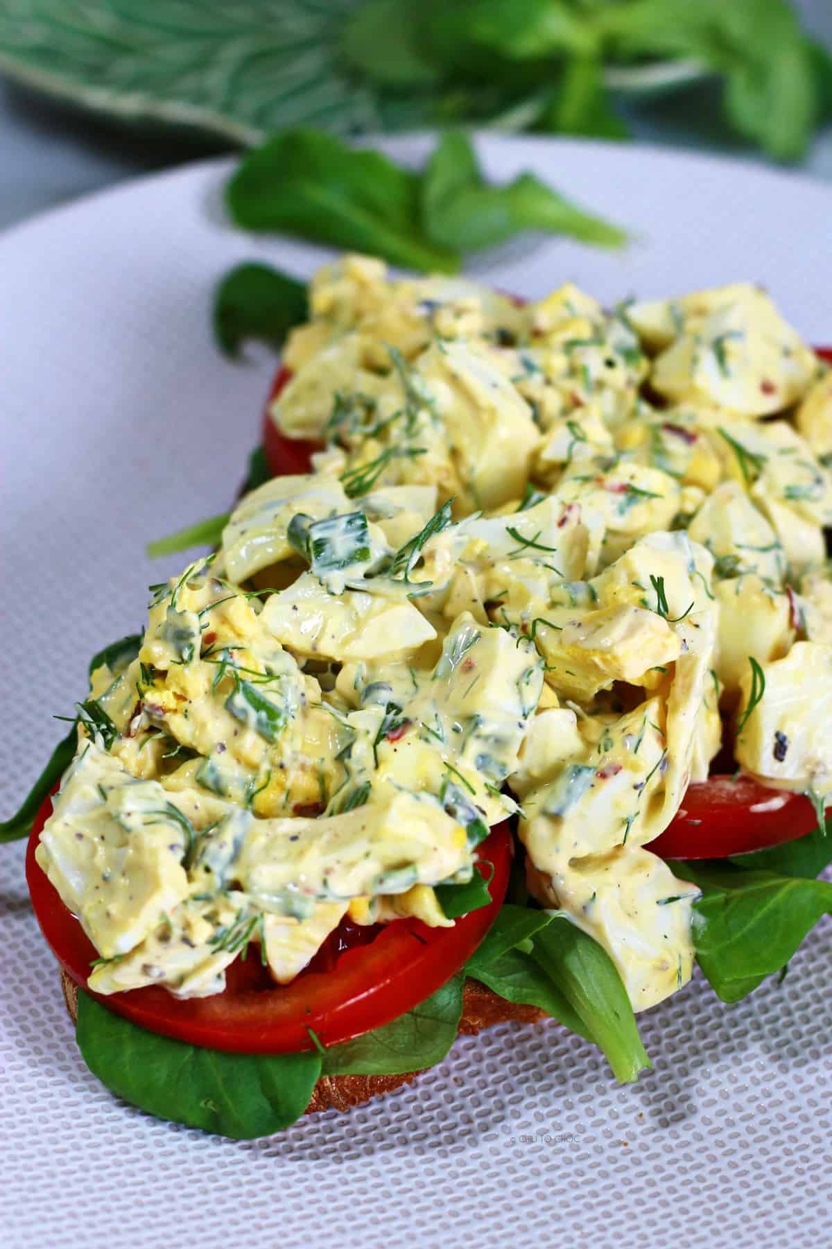 An open egg salad sandwich on a white plate.