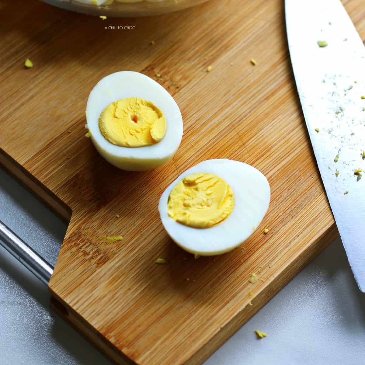 Sliced hard boiled egg on a wooden board with a knife on the side.