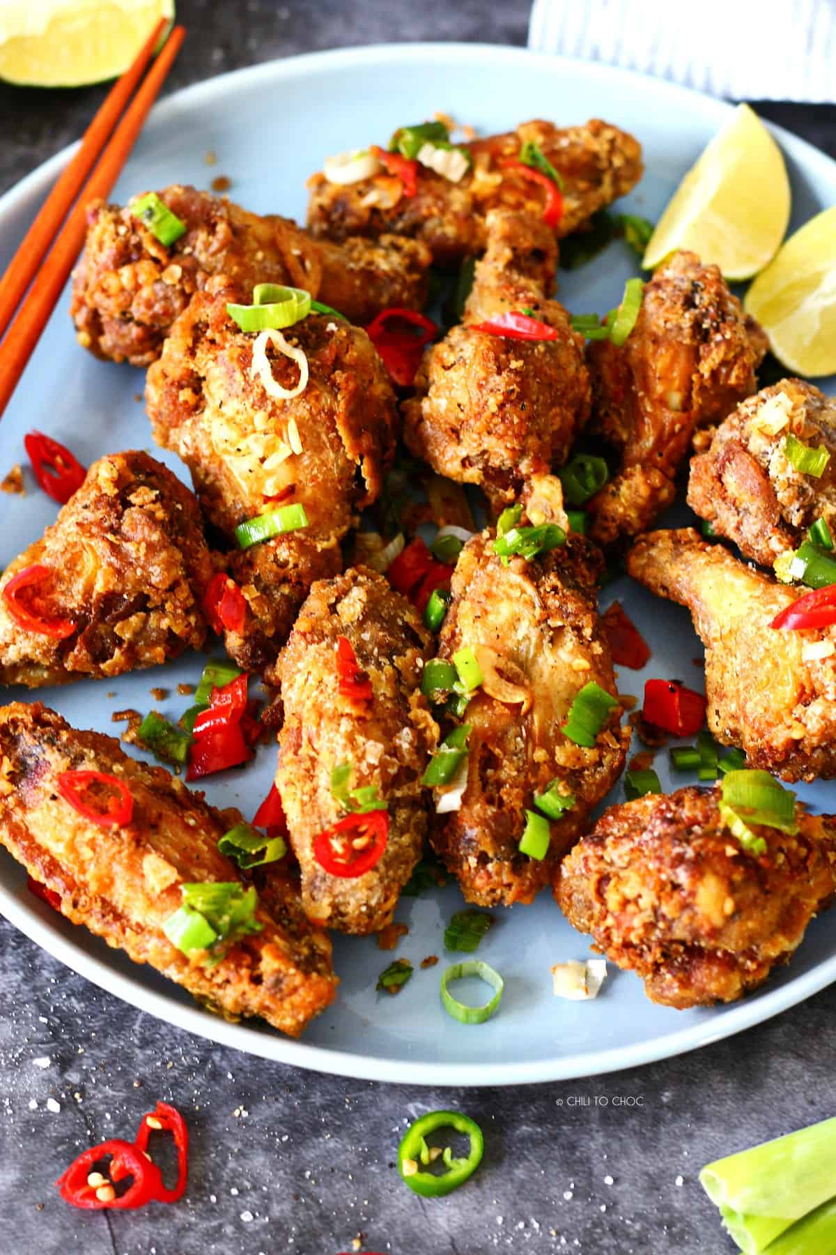 Salt and pepper chicken wings garnished with sliced spring onion, garlic and chilies and lemon wedges on the side.