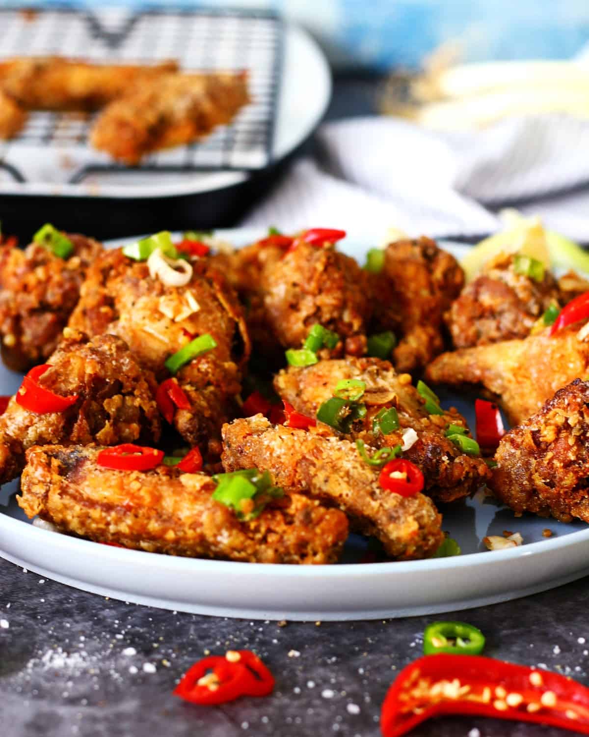 Salt and pepper chicken wings on a plate with garnish and sliced chilies in front.