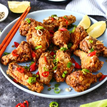 Salt and Pepper Chicken Wings on a blue plate with stir fried garlic, chili and spring onion on top.