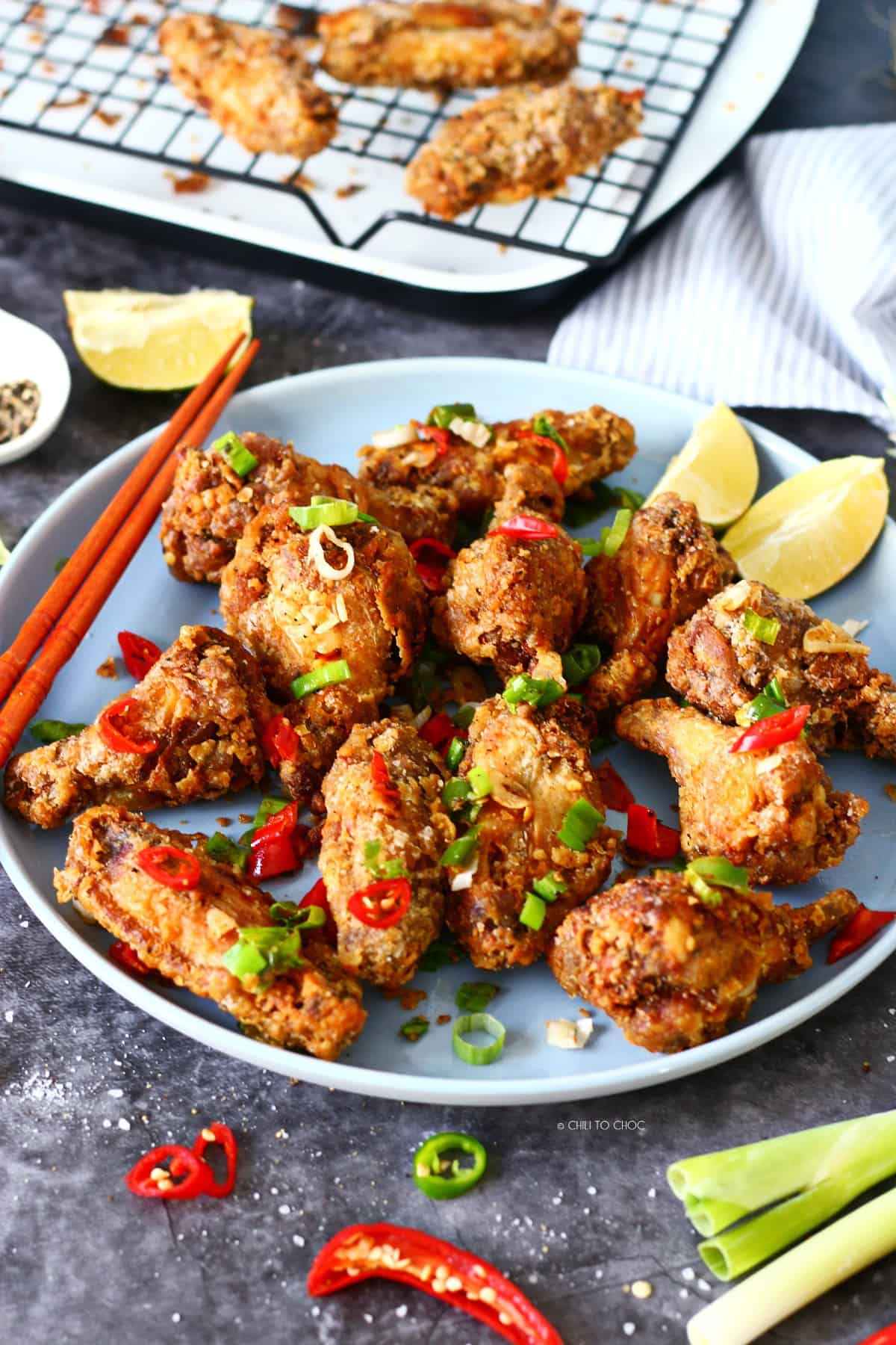 Chinese salt and pepper chicken wings on a plate with chopsticks on the side and chilies and toasted garlic for garnish.