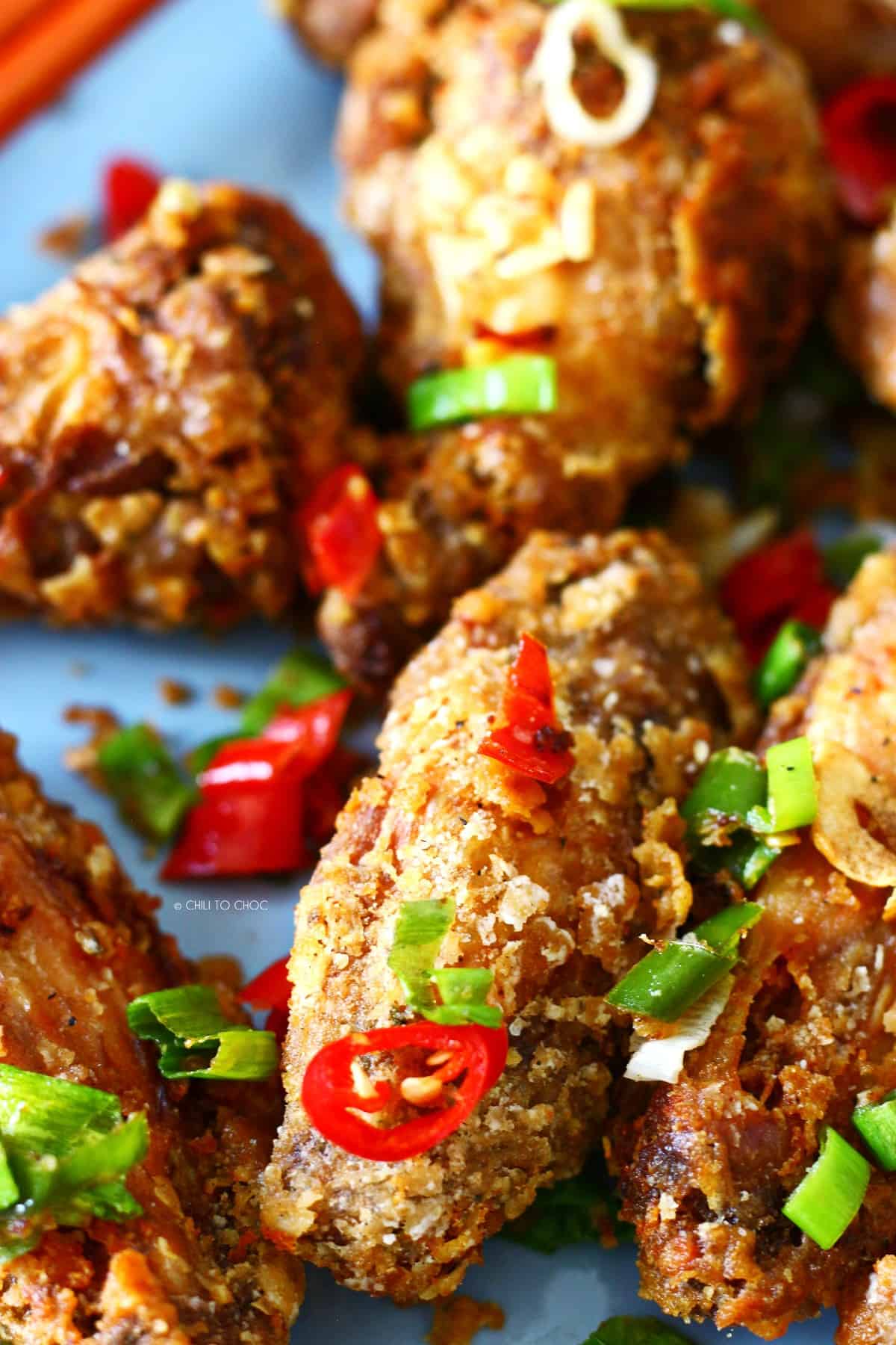 Closeup of salt and pepper chicken wing with red chili and spring onion garnish.