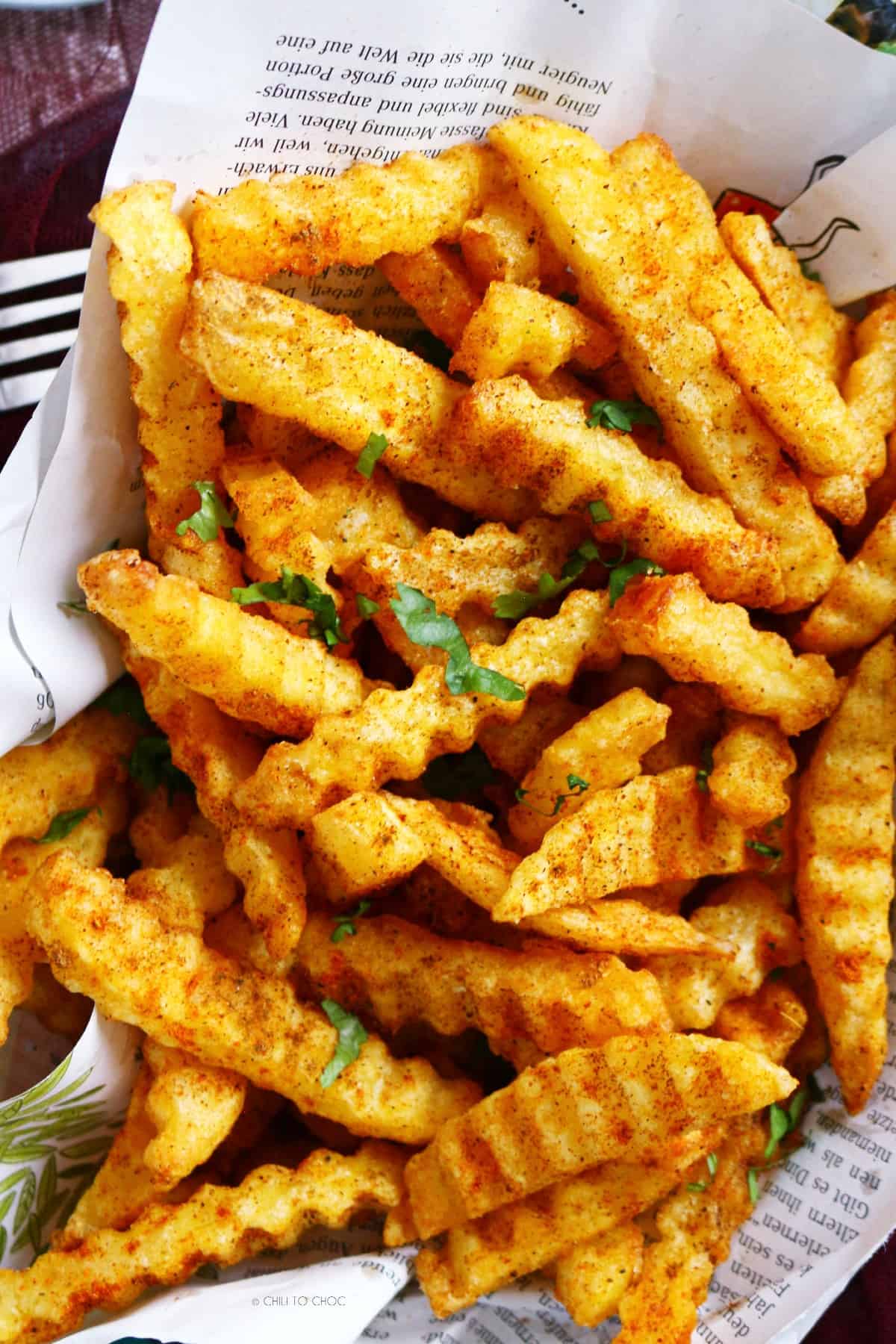 Masala fries on a magazine paper garnished with fresh coriander.