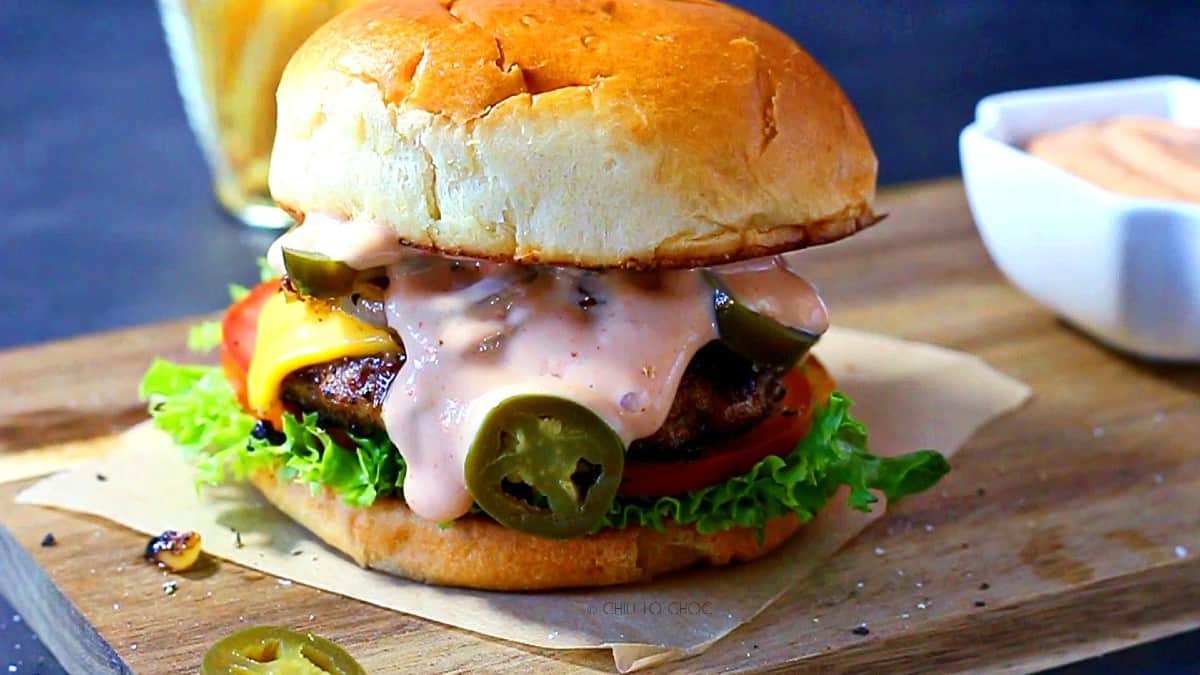 Beef burger oozing with sauce on a wooden board.