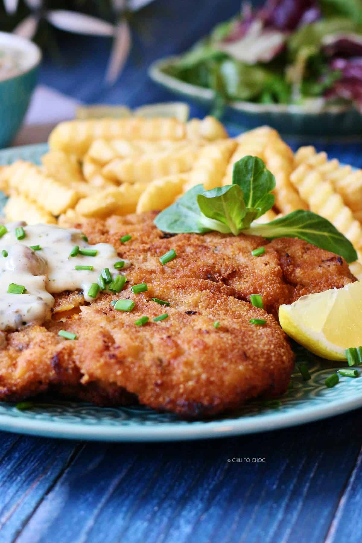 Chicken schnitzel with fries and a salad on the back.