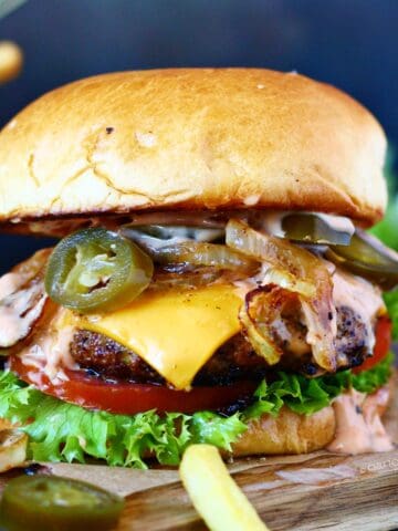 The ultimate cheeseburger with pickled jalapenos on a wooden board.