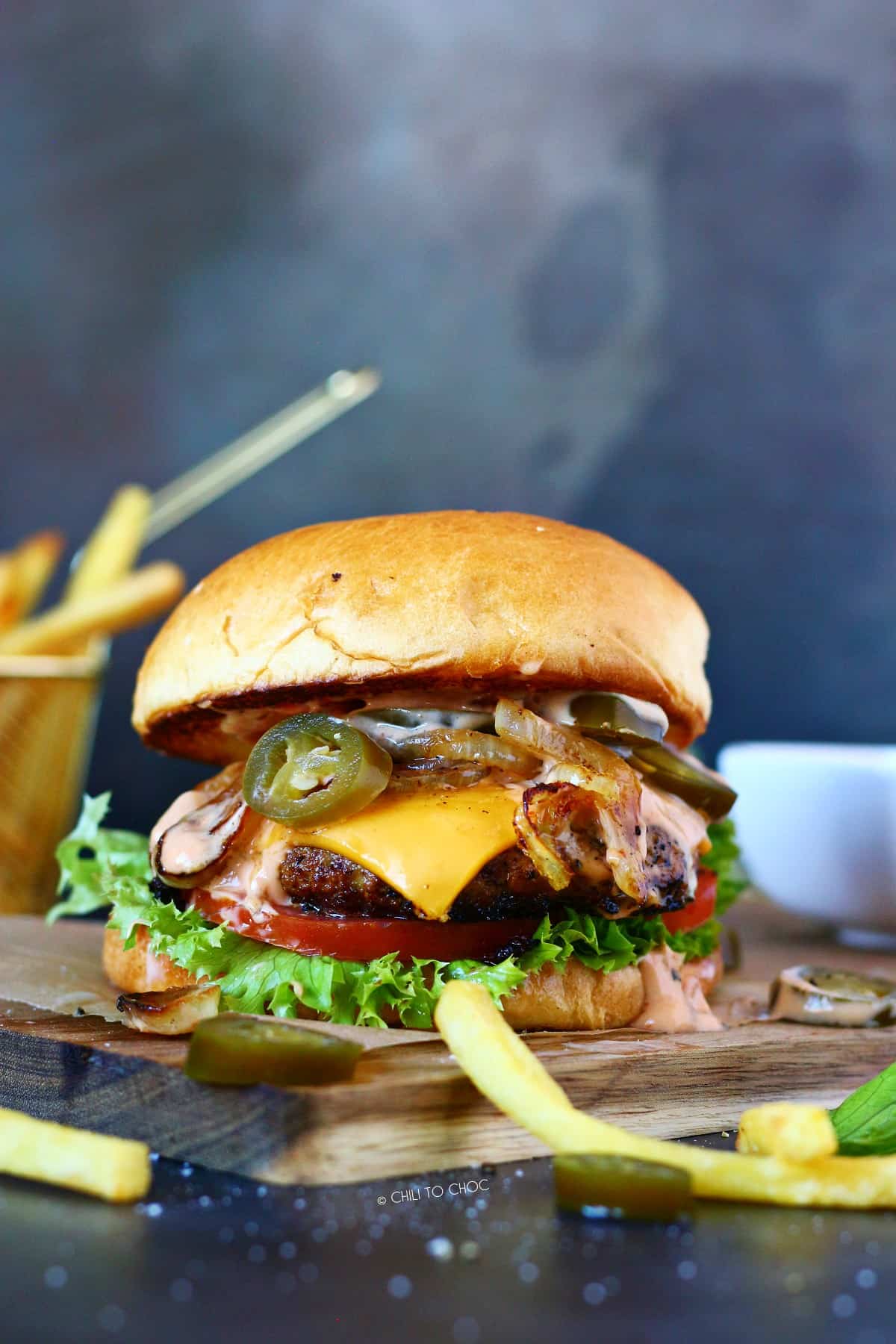 Beef burger with pickled jalapenos on a wooden board with fries on the front.