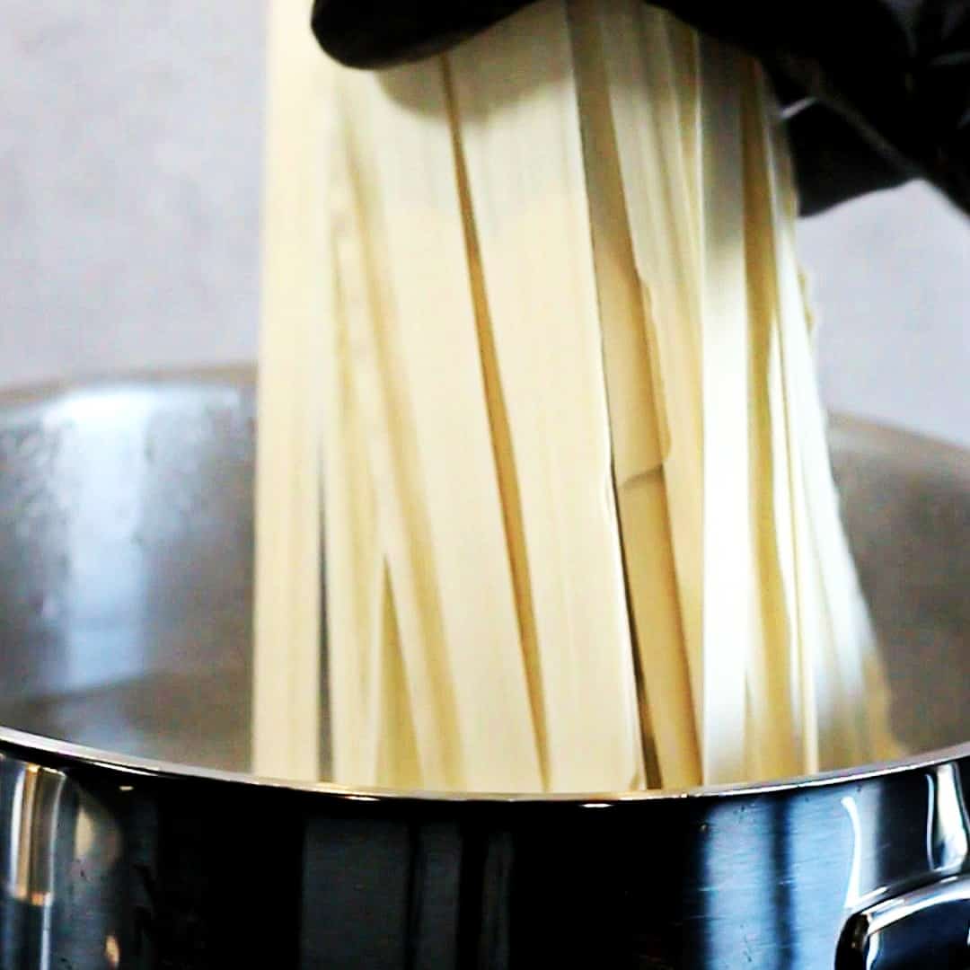 Noodles going in a pot with water.