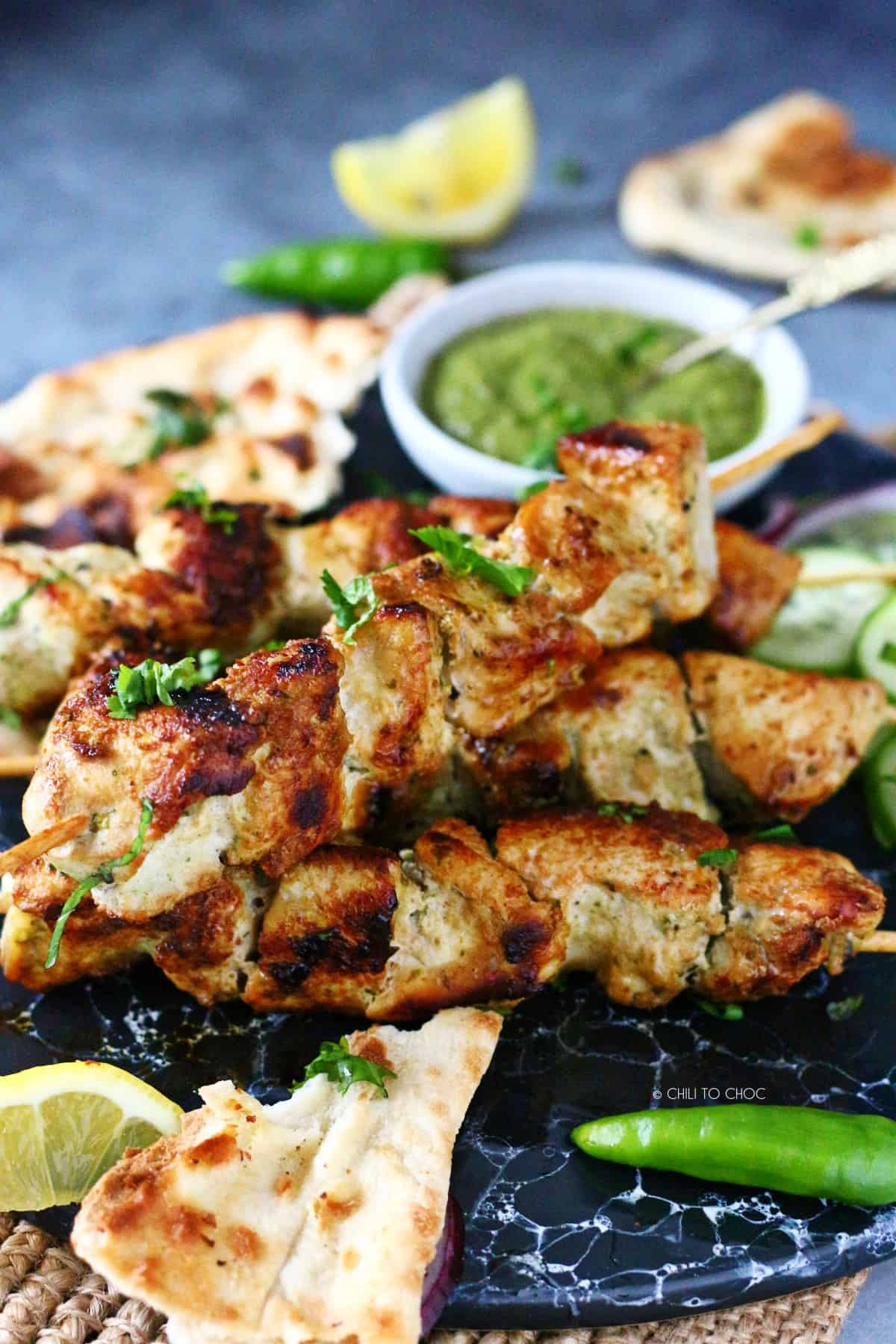 Malai tikka skewers on a marble dish with garnishes on the side.