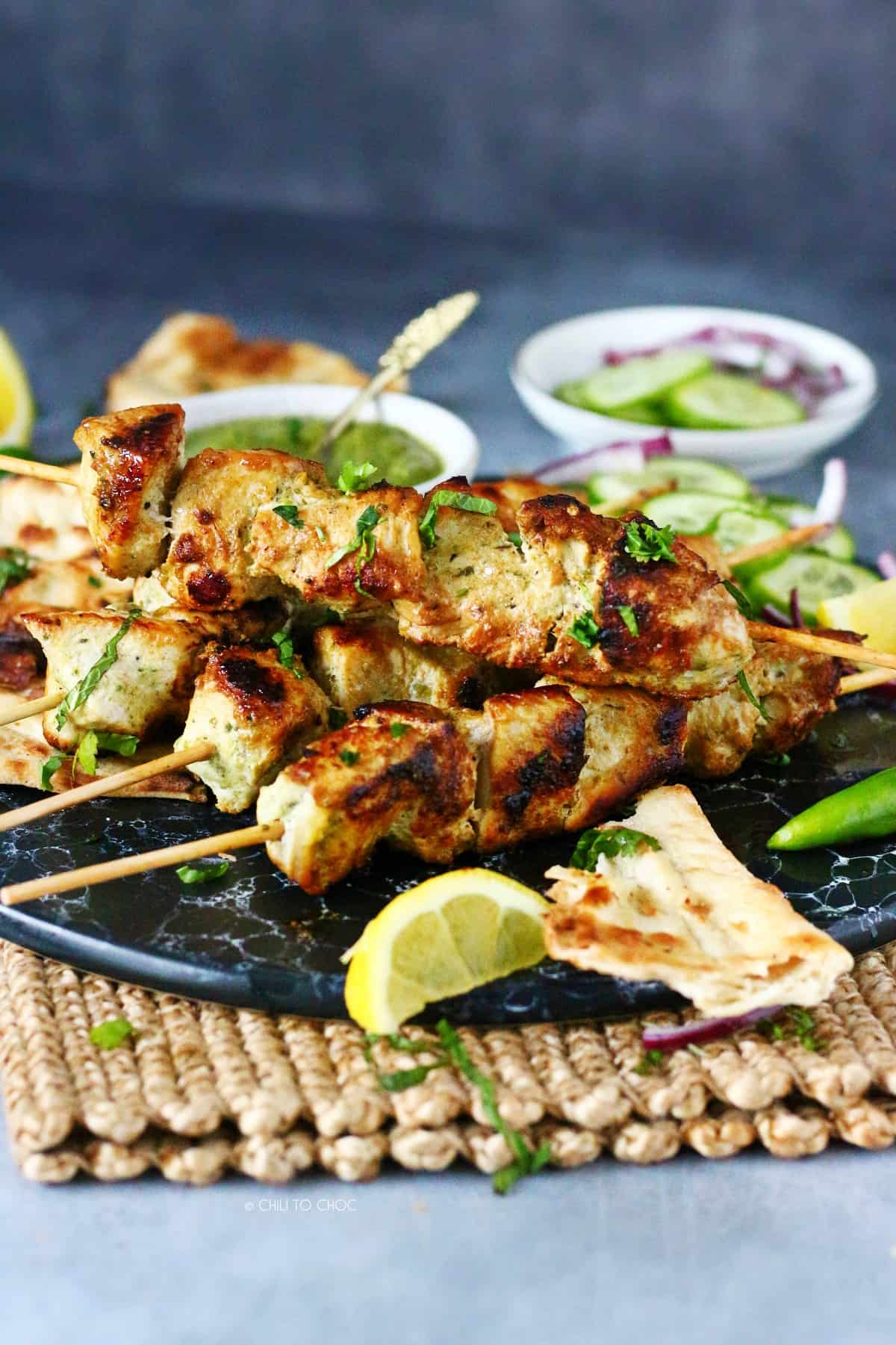 Chicken malai boti skewers stacked on each other with a piece of naan on the side.