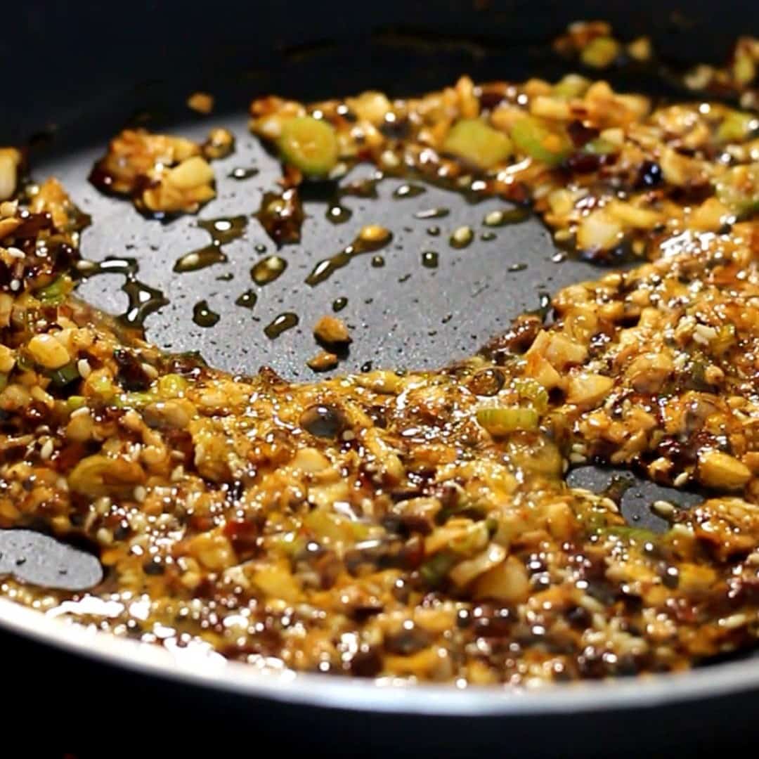 Oil in pan with diced garlic, green onion, chili flakes and sesame seeds.