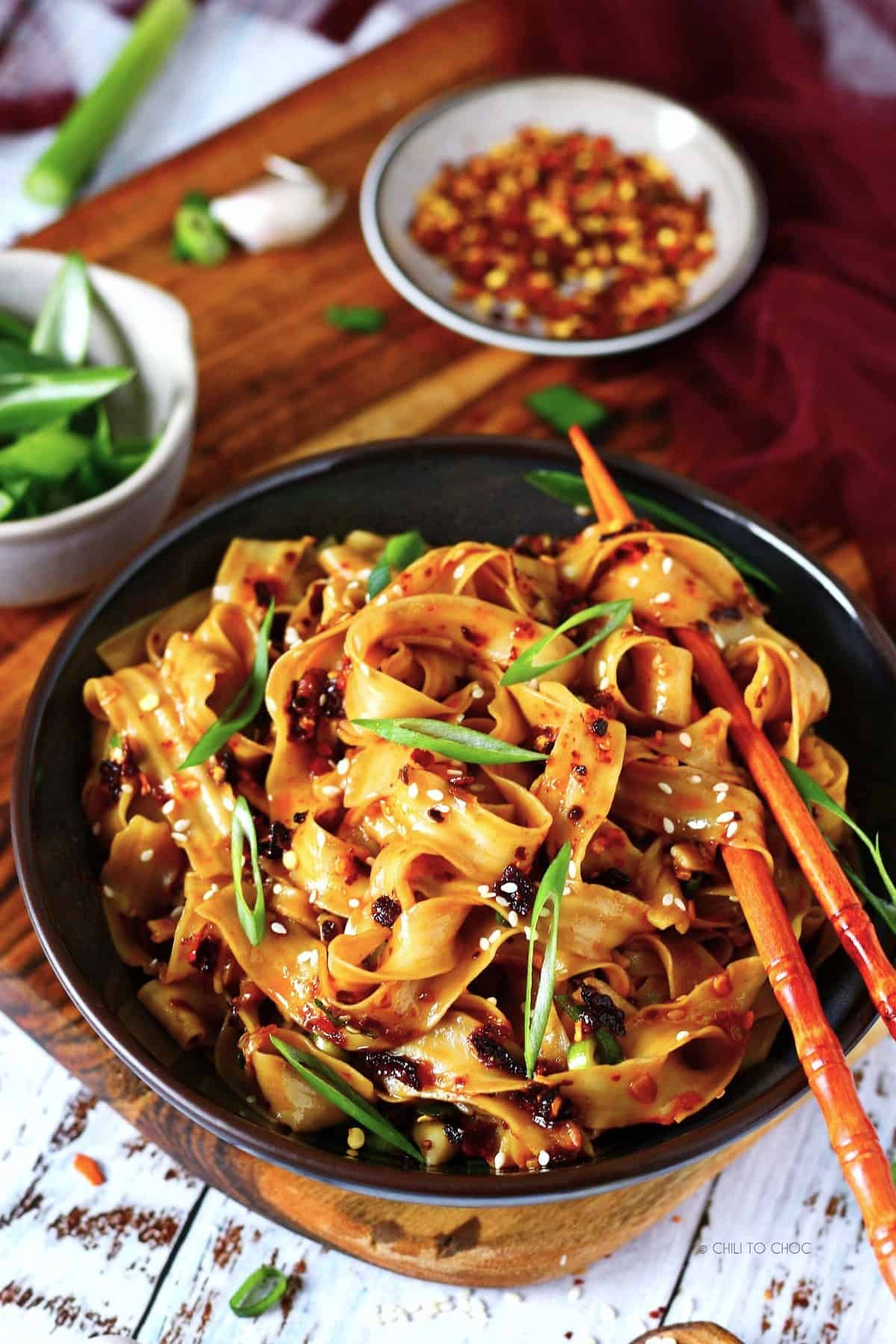 Garlic chili oil noodles with chopsticks in a bowl with ingredients at the back.