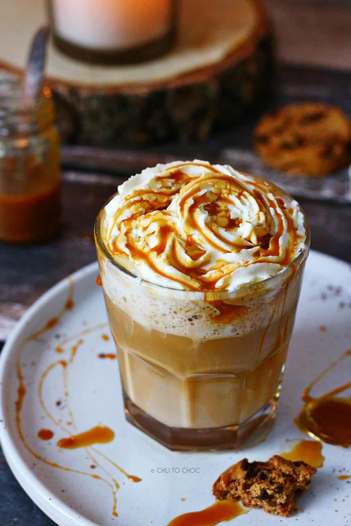 Caramel latte with whipped cream and caramel sauce on a white place with a spoon on the side.