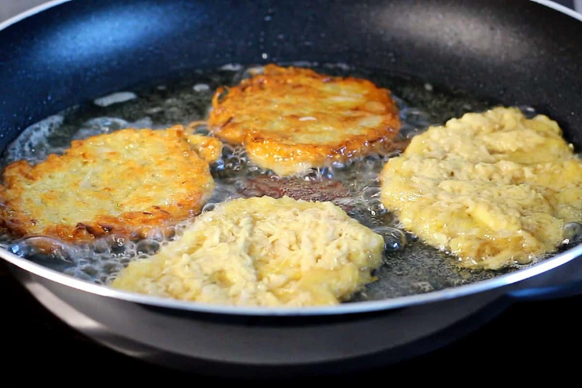 Frying potato pancake in oil in a black pan.