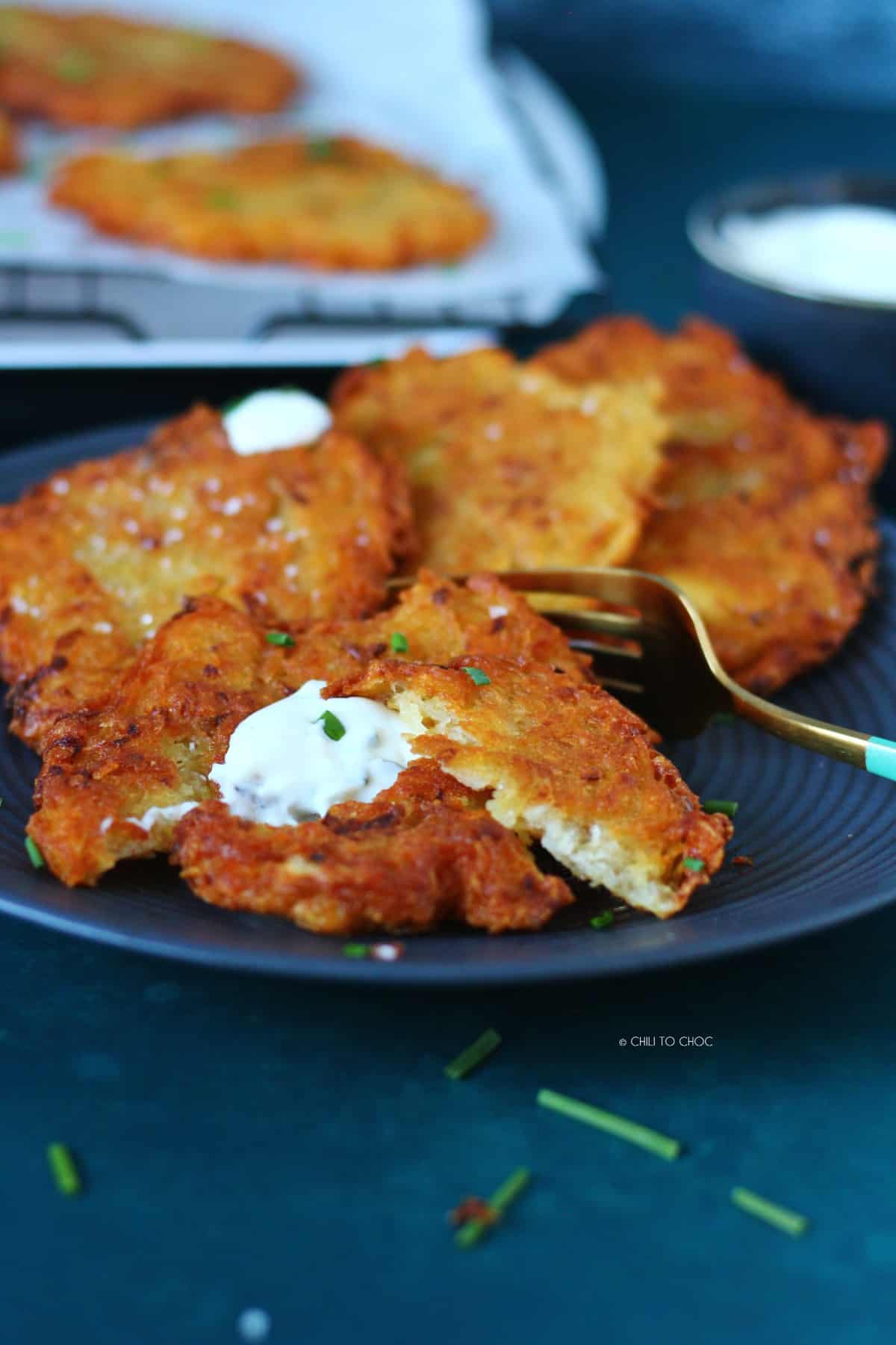 Potato pancakes on a plate with one fritter cut up.