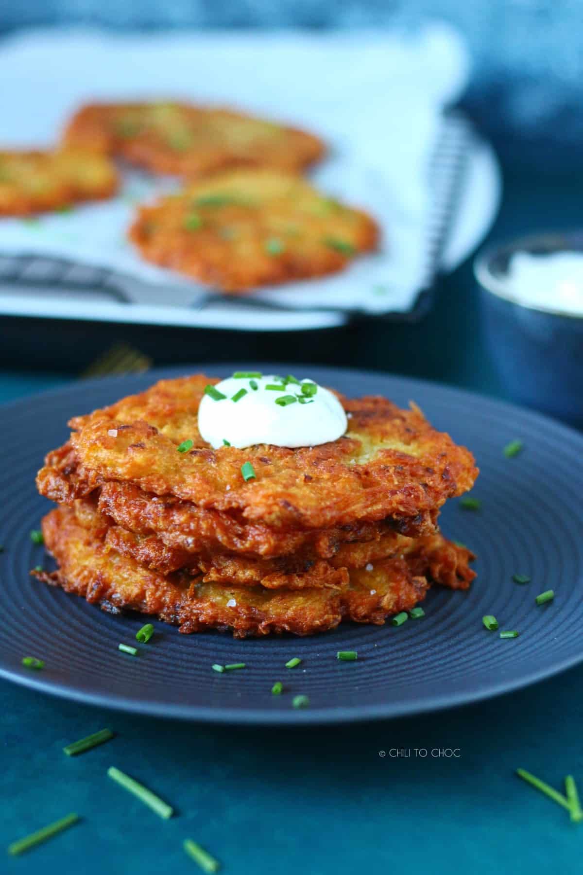 A stack of kartoffelpuffer topped with sour cream and chopped chives with some pancakes at the pack.