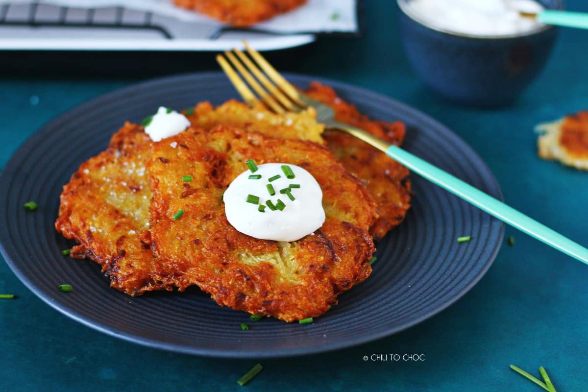 Potato pancakes on a black plate garnished with sour cream and a fork on the side.