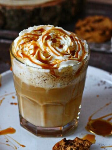 Caramel Latte in a clear glass on a white plate drizzled with caramel sauce.