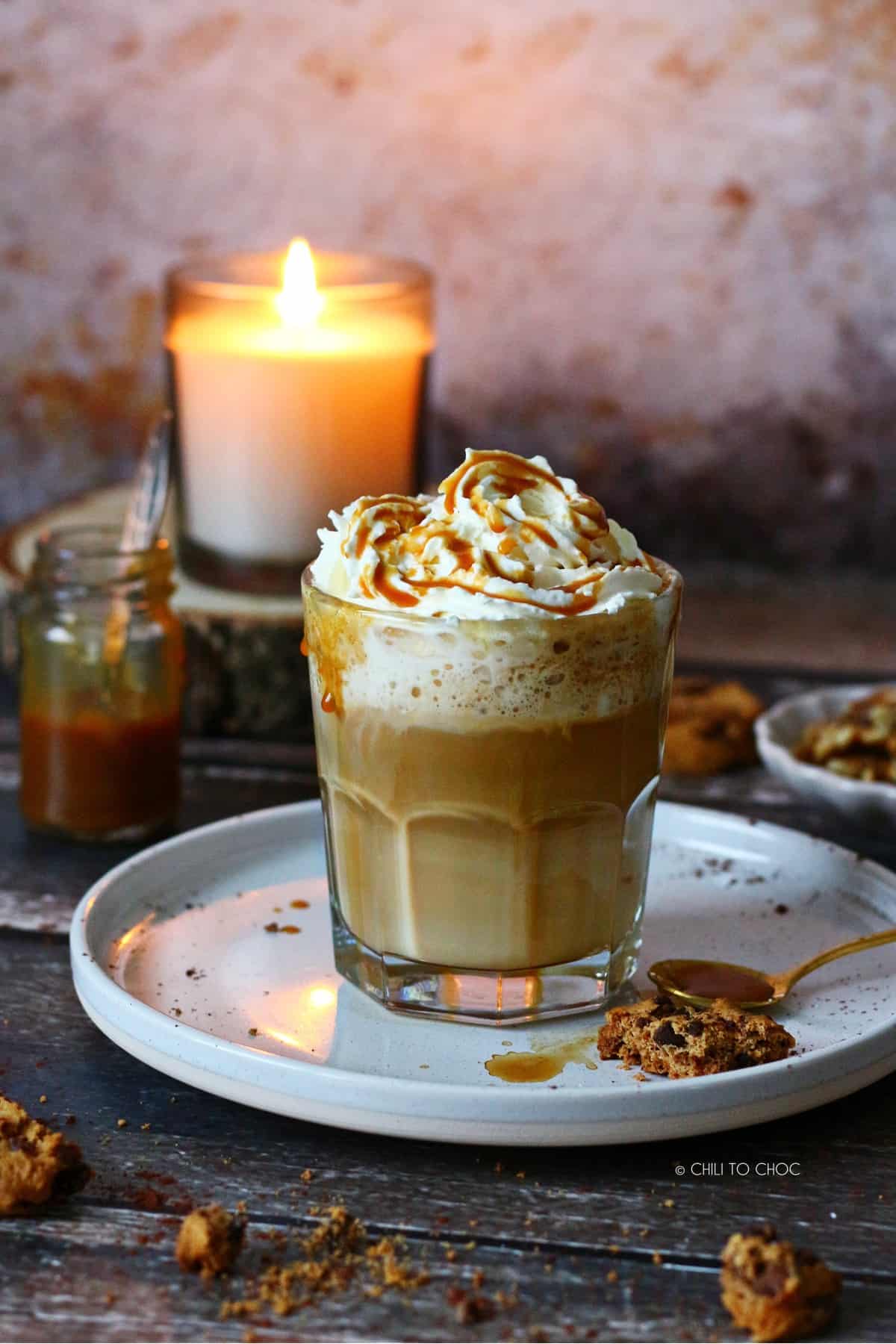 Caramel latte topped with whipped cream and caramel sauce and a candle burning behind the glass.