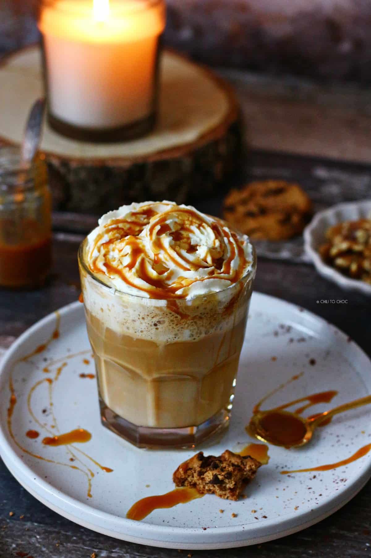 Caramel latte on a place smeared with caramel sauce and walnuts and cookies around it.