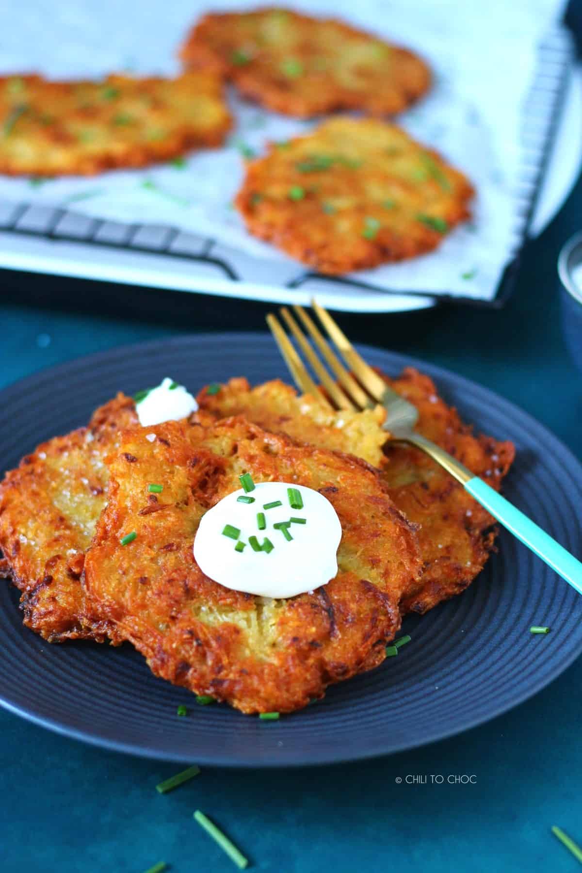 Set of German potato pancakes on a plate topped with sour cream and chopped chives with a fork on the side.