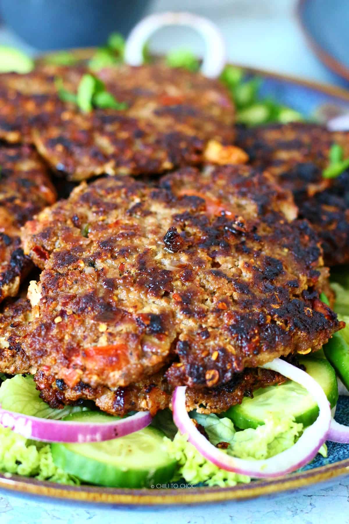 Chapli kabab on a bed of lettuce, sliced cucumber and red onion rings.