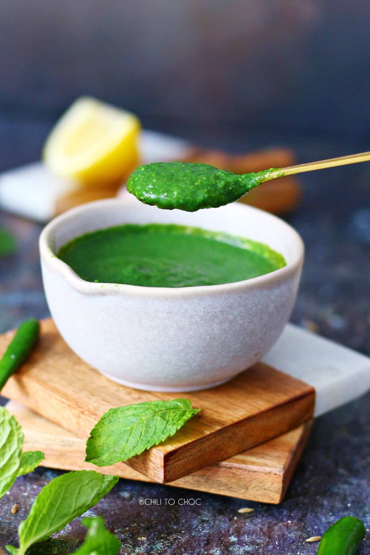 Picking up green chutney in a spoon from the bowl.