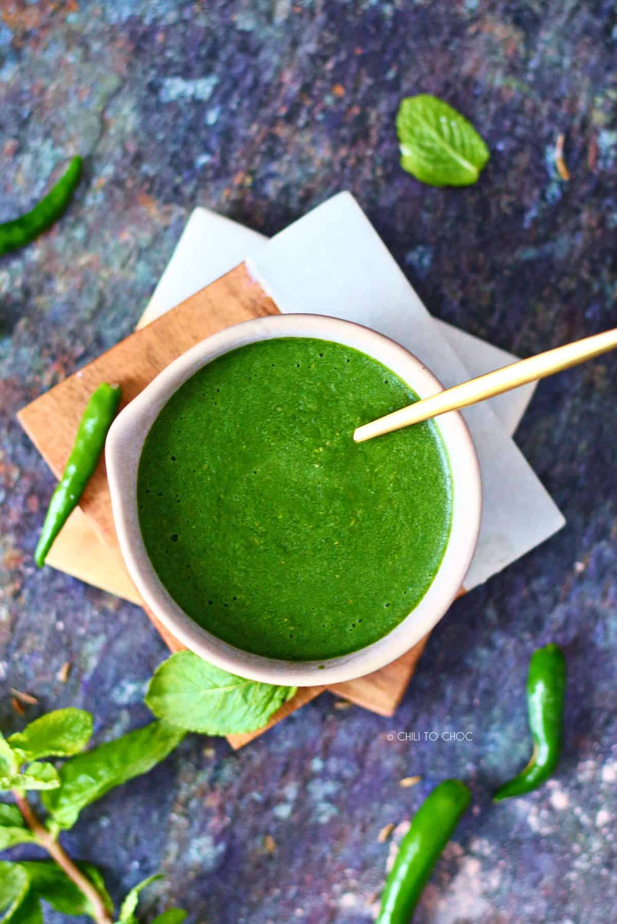 Green chutney in a bowl on two coasters surrounded by its ingredients.