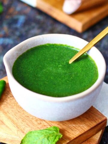 Green chutney in a small bowl with a gold spoon inside.