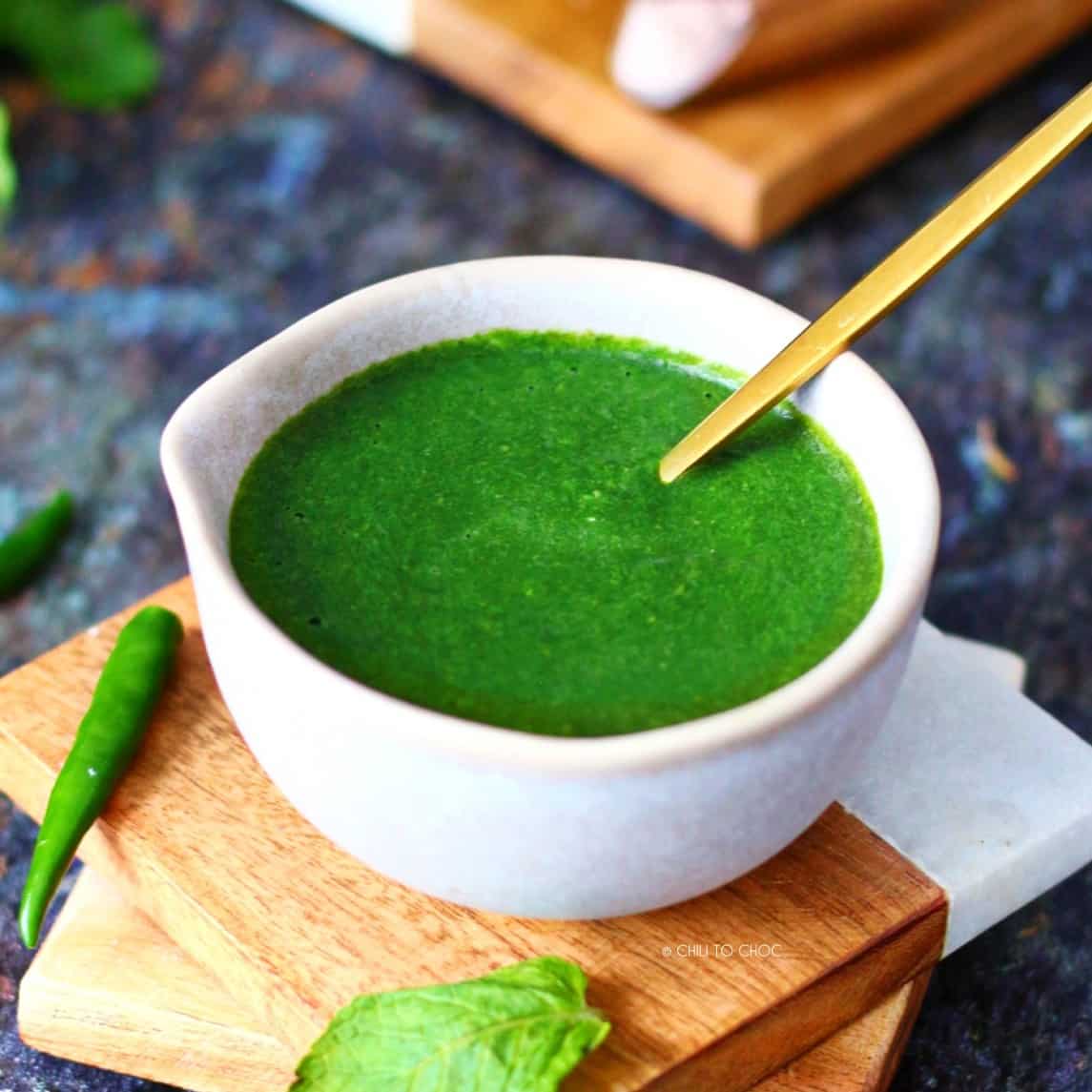 Green chutney in a small bowl with a gold spoon inside.
