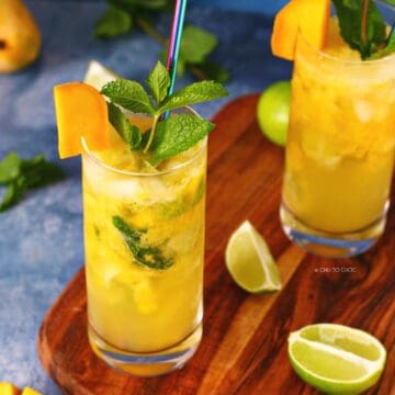 Two glasses of mango mojito on a wooden board with lime wedges on it.