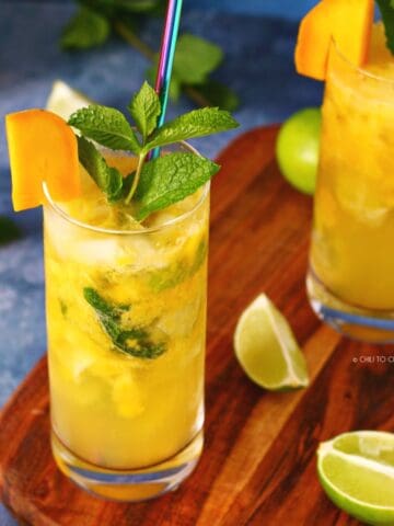 Two glasses of mango mojito on a wooden board with lime wedges on it.