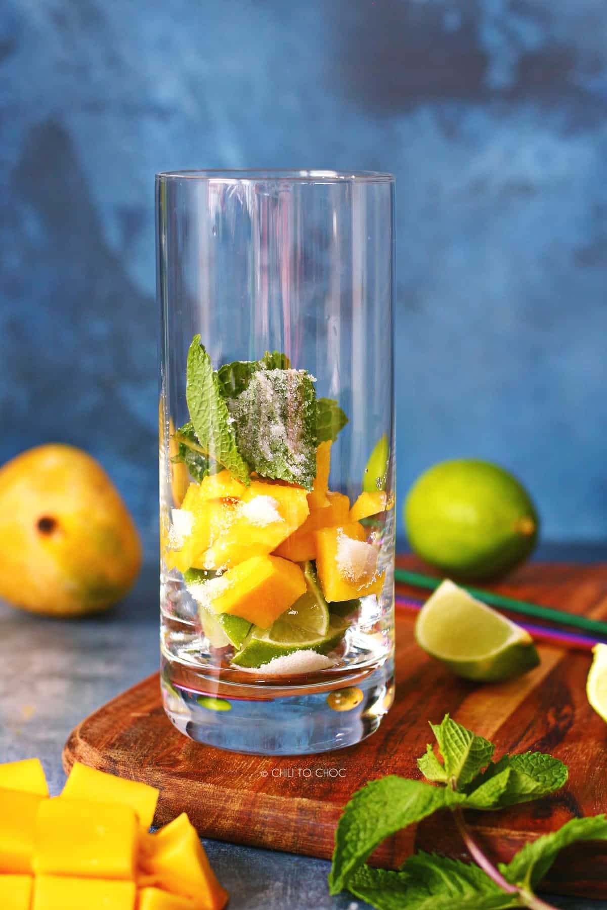 Lime quarters, mango chunks, mint leaves and sugar in a highball glass.
