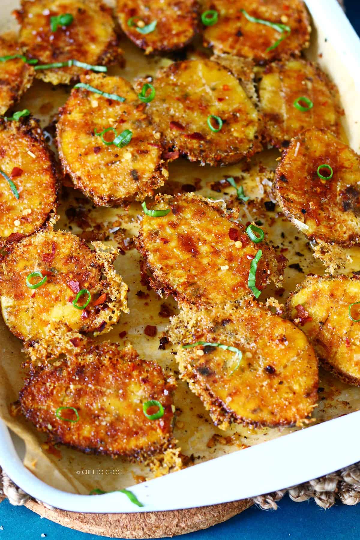 Crispy Parmesan crusted potatoes on a baking tray garnished with chopped green onion.