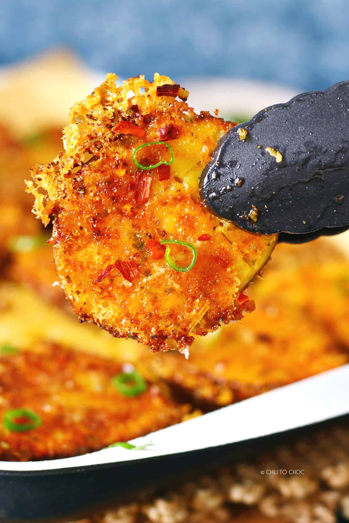 A pair of black tongs holding one Parmesan roasted potato.