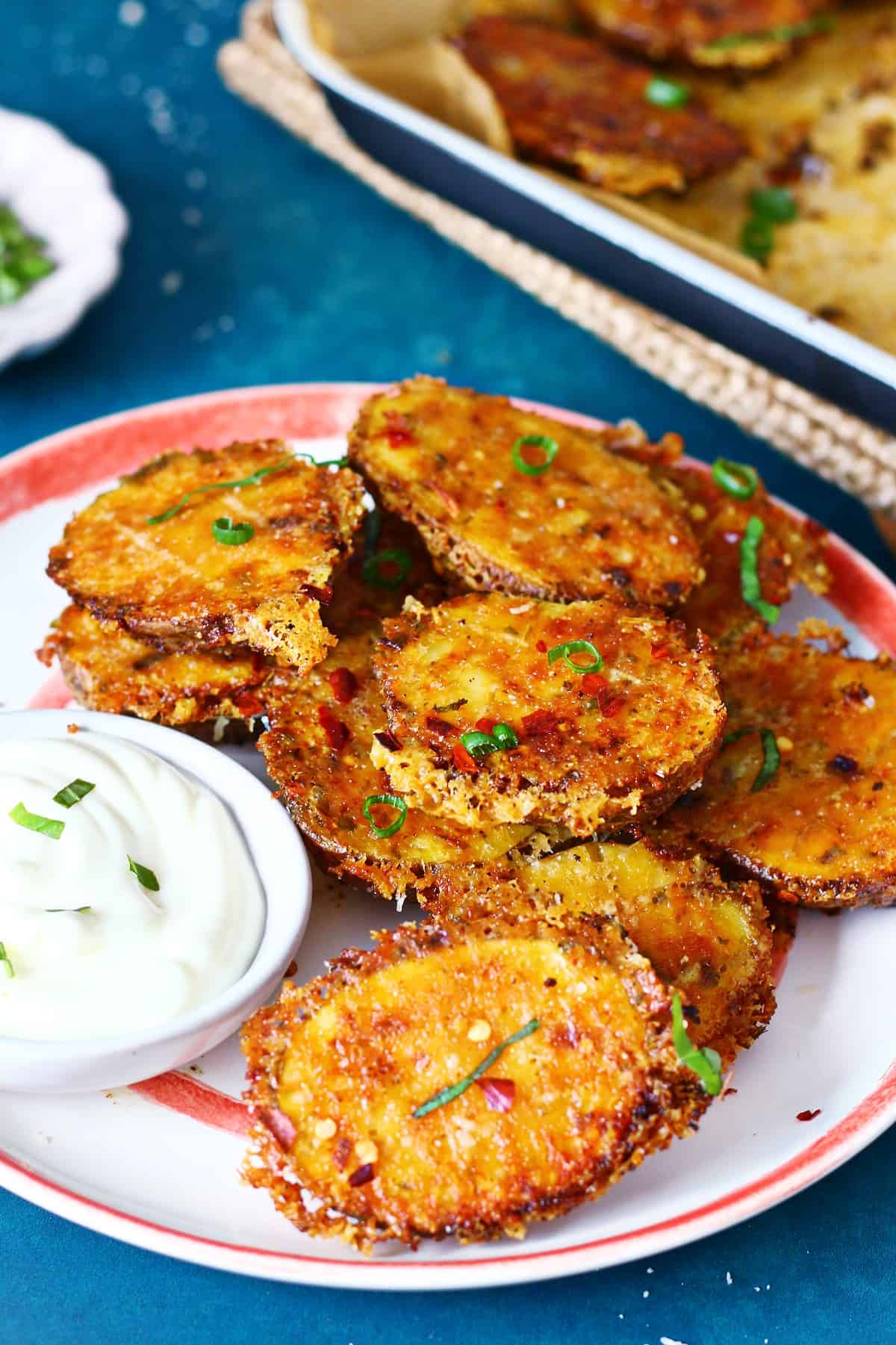 Parmesan potatoes stacked on top of each on a plate with garlic aioli on the side.