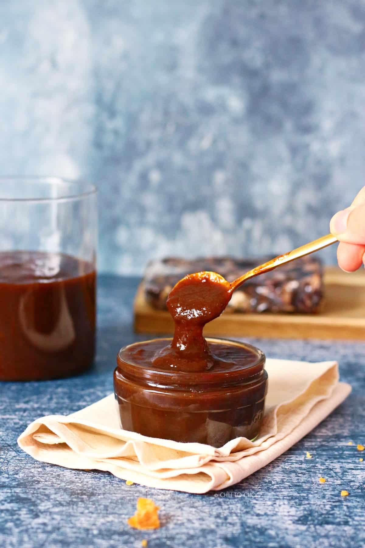 Pouring tamarind chutney from a spoon in a glass bowl.