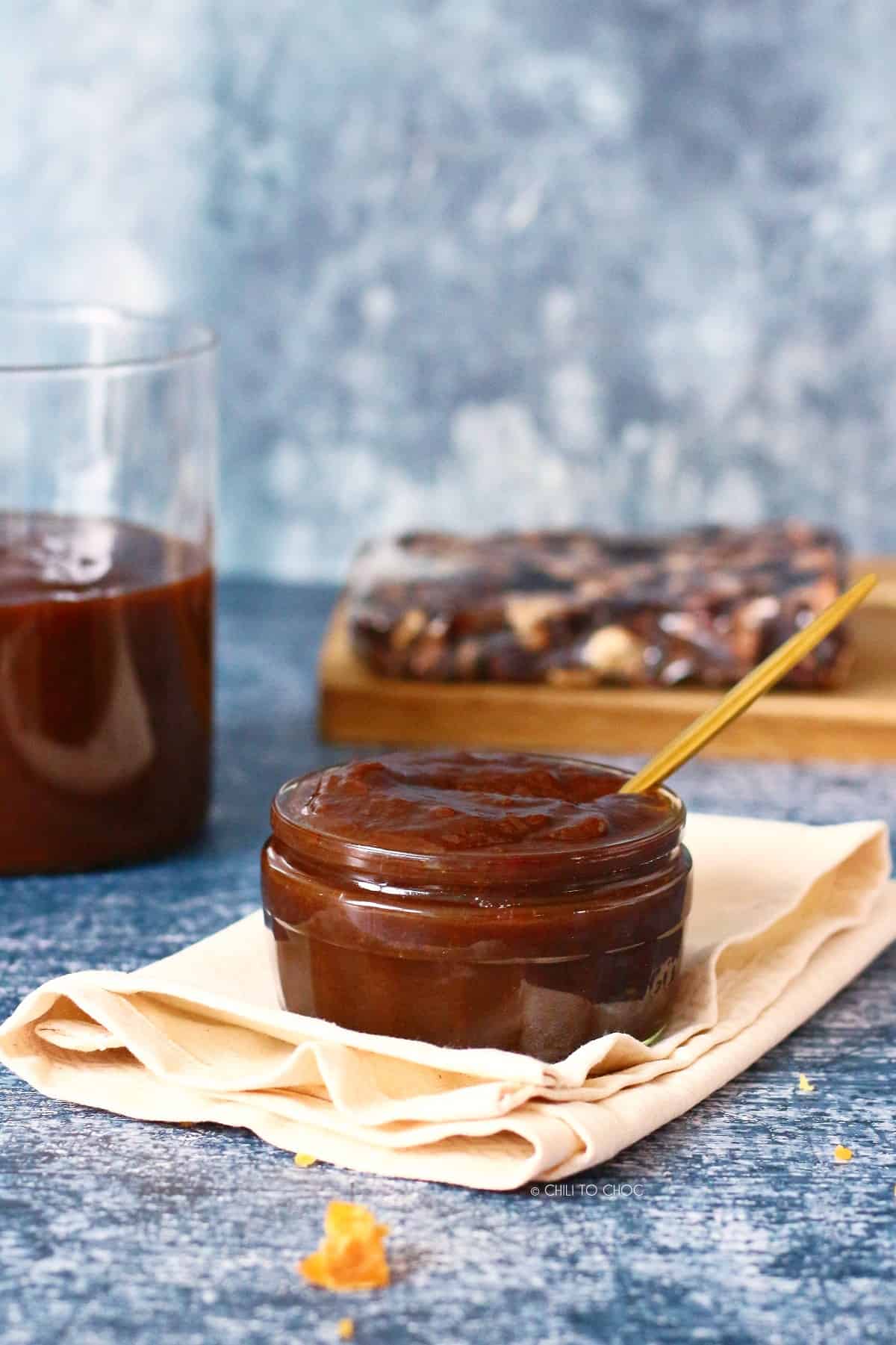 Tamarind dip bowl in the front with a glass jar with chutney and a tamarind block at the back.