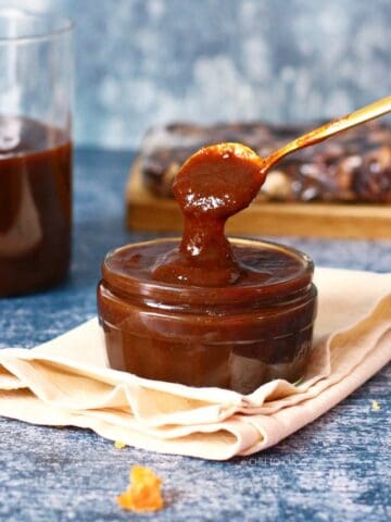 A bowl of tamarind chutney on a piece of cloth with spoon dropping chutney into it.