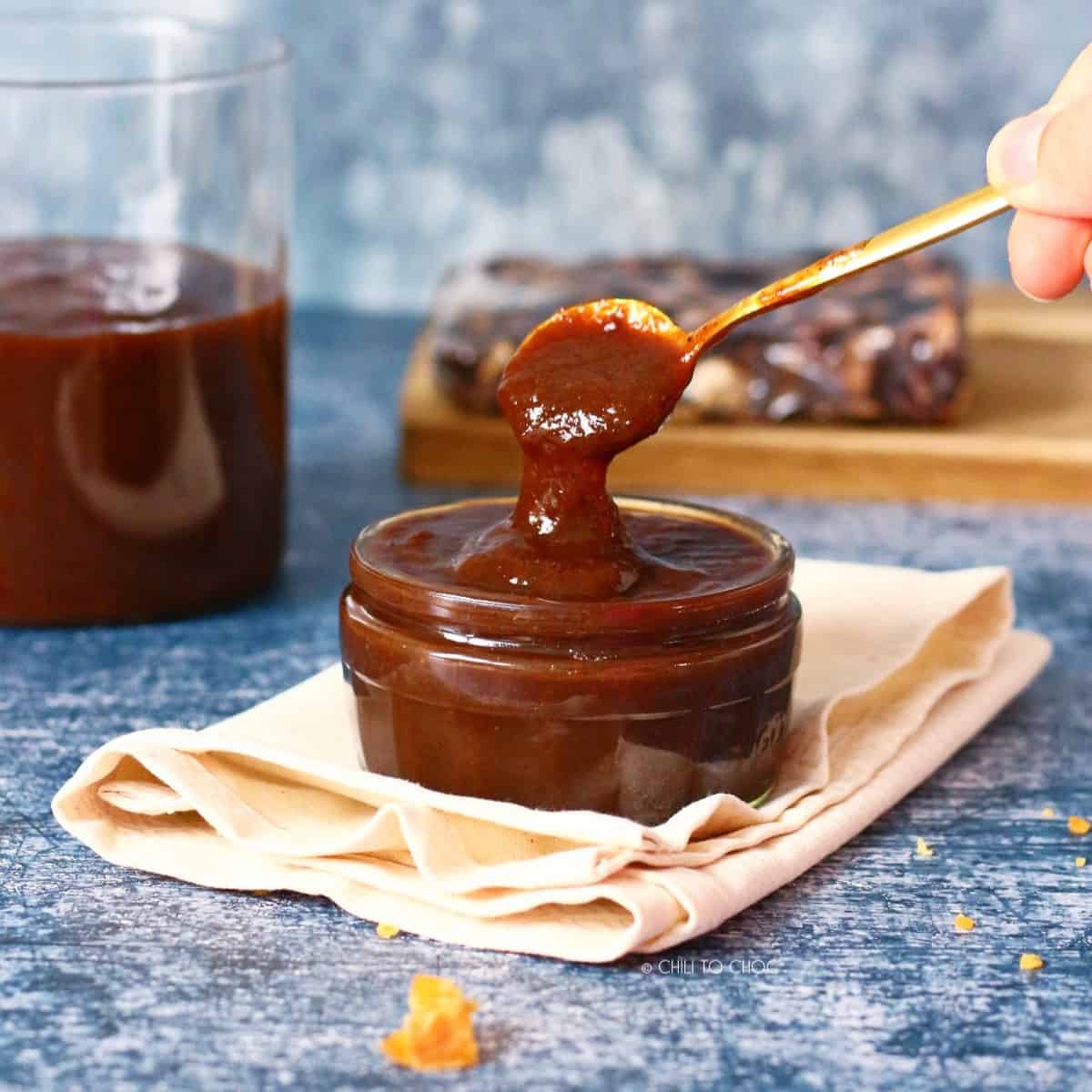 A bowl of tamarind chutney on a piece of cloth with spoon dropping chutney into it.