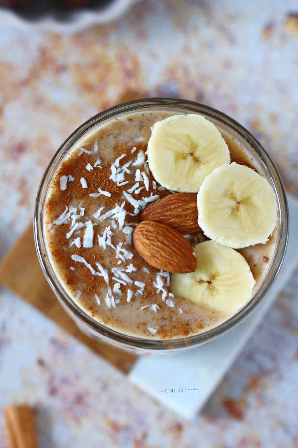 The top of the date smoothie garnishes with sliced bananas, whole almonds, cinnamon powder and desiccated coconut.