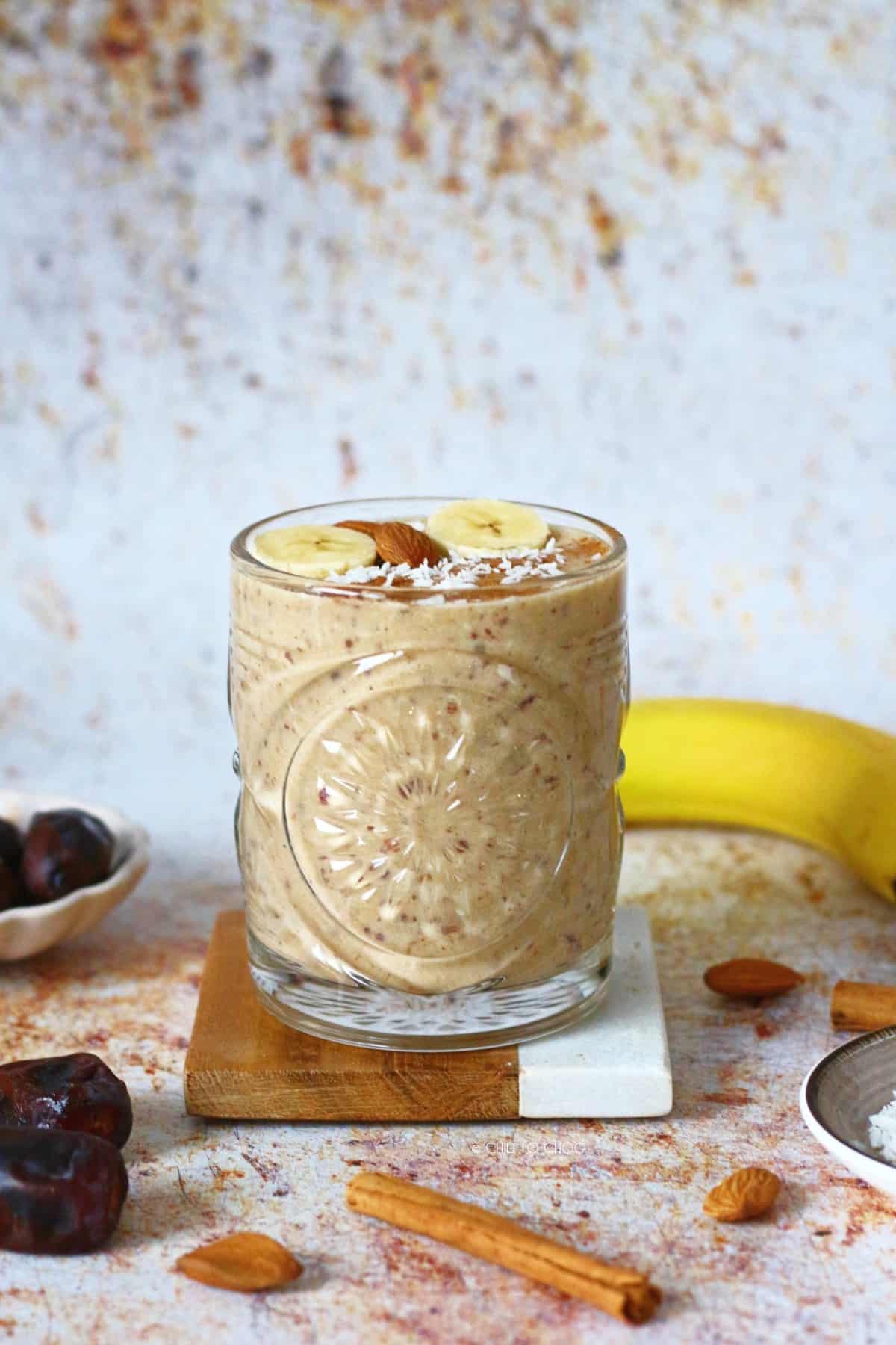 Banana Date Smoothie in a glass on a coaster surrounded by all the ingredients.