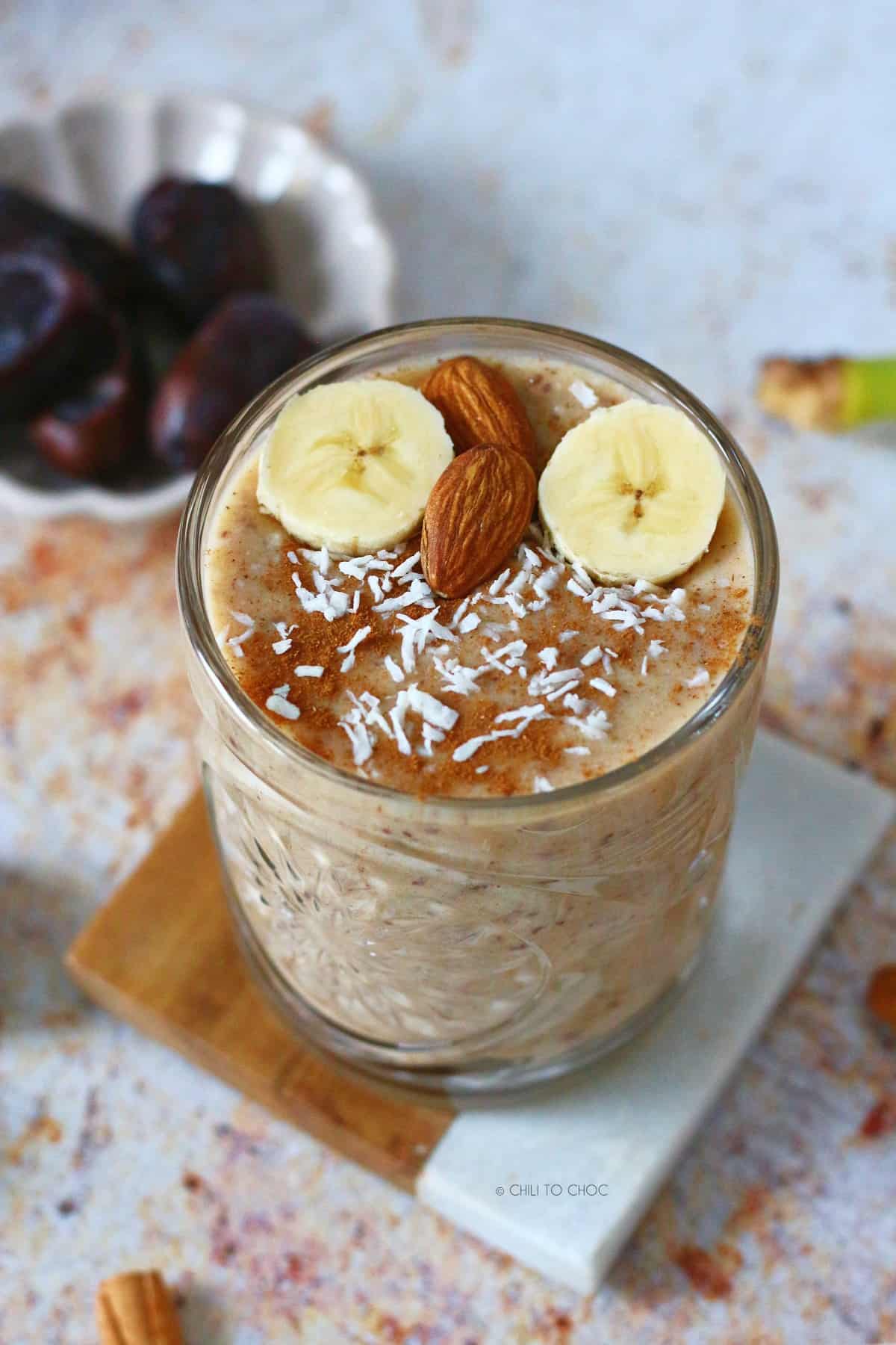 Date Smoothie in a glass with its garnishes showing and a small plate of dates at the back.