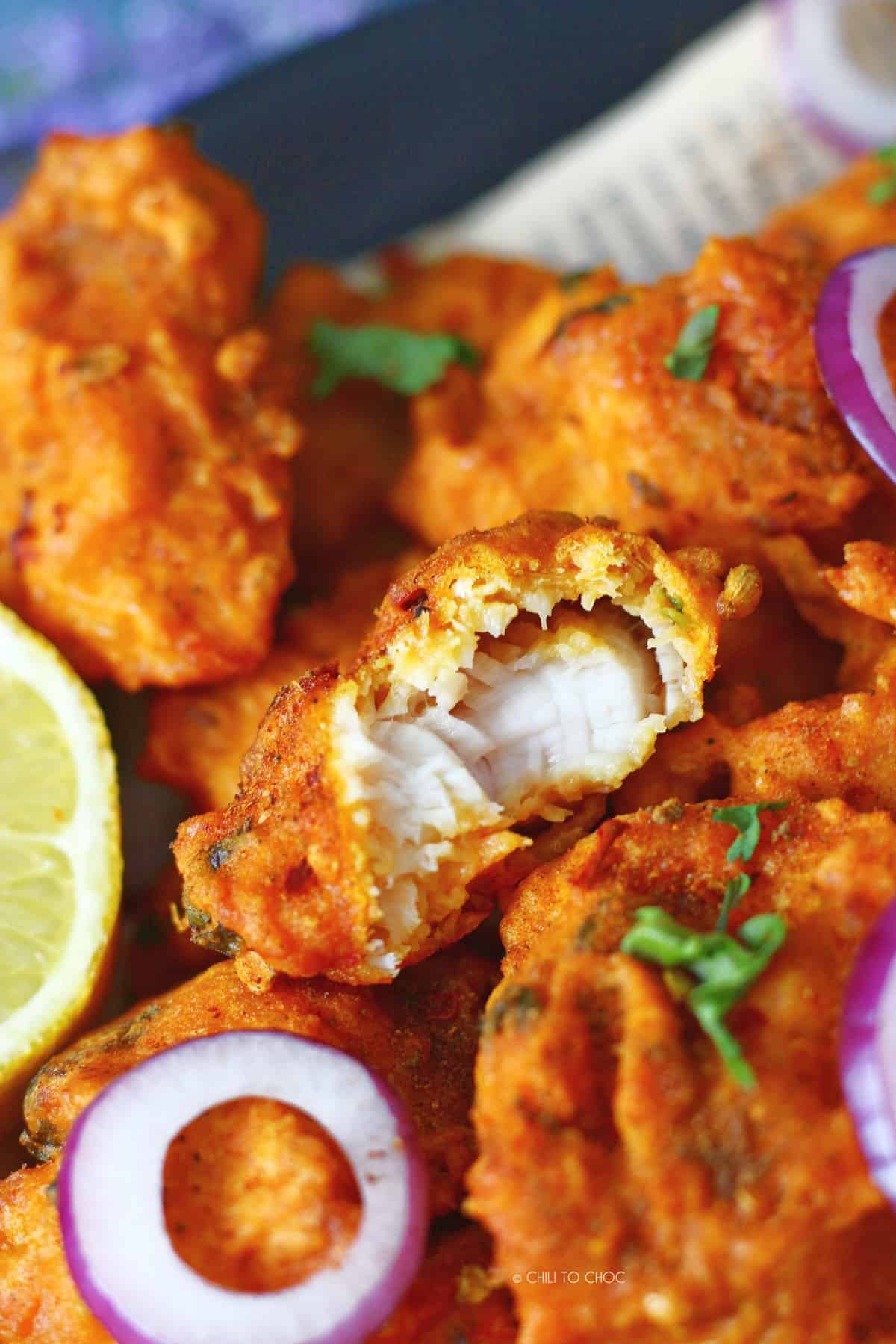 A piece of fish pakora broken in half, stacked on other fish fritters.