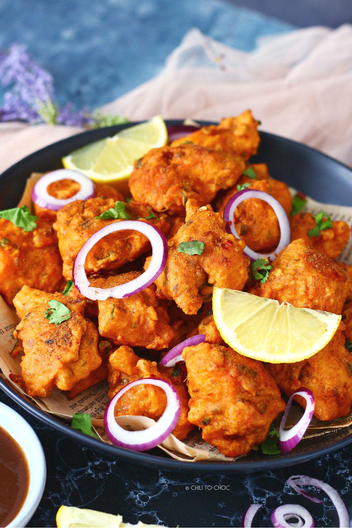 Fish pakoras garnished with onion rings, lemon wedges and fresh coriander.